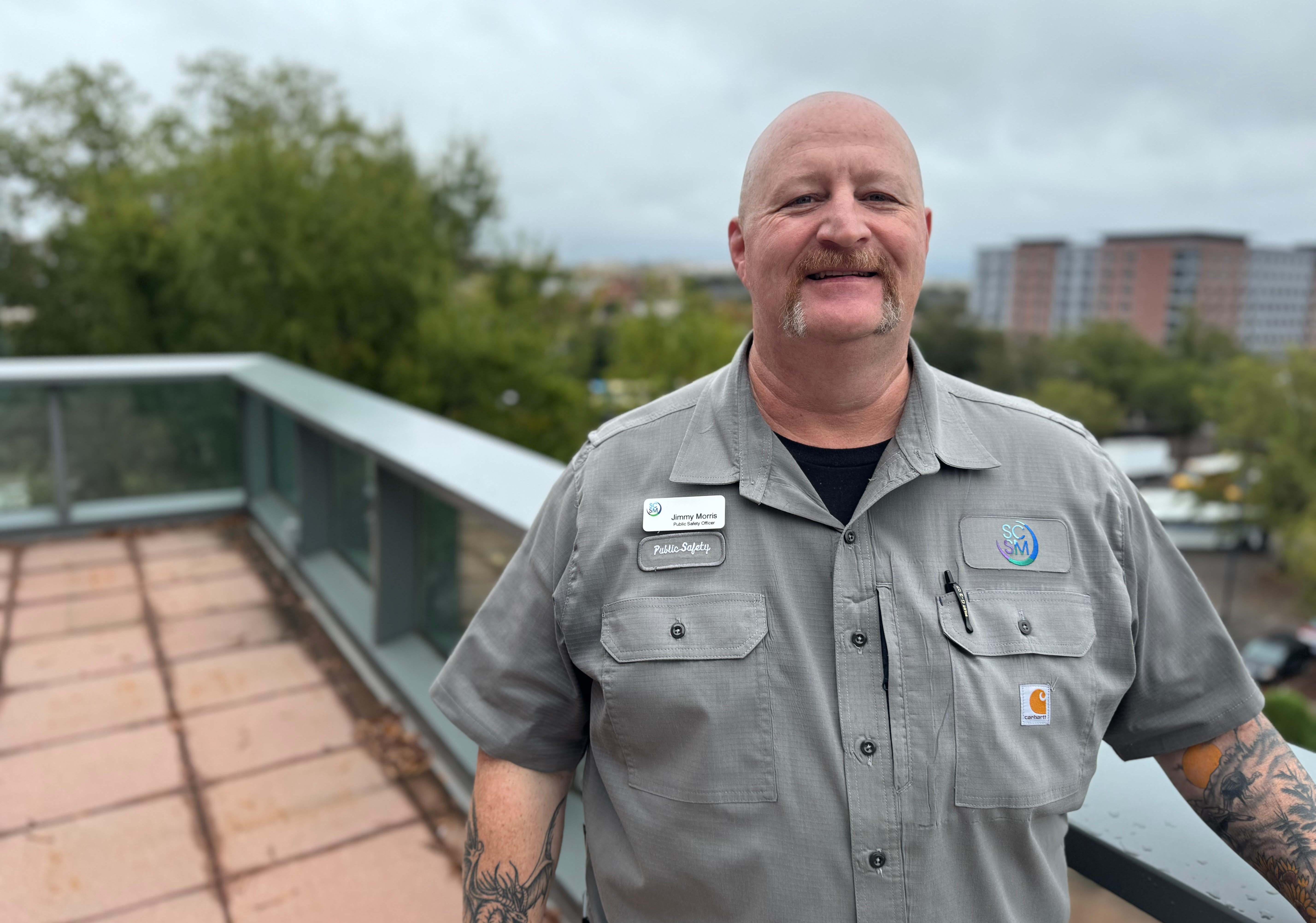 Man stands on balcony wearing a taupe shirt and nametag